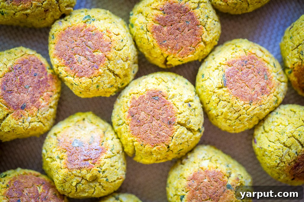 Several golden-brown roasted butternut squash falafel bites neatly arranged on a baking sheet, fresh out of the oven and ready to be served.