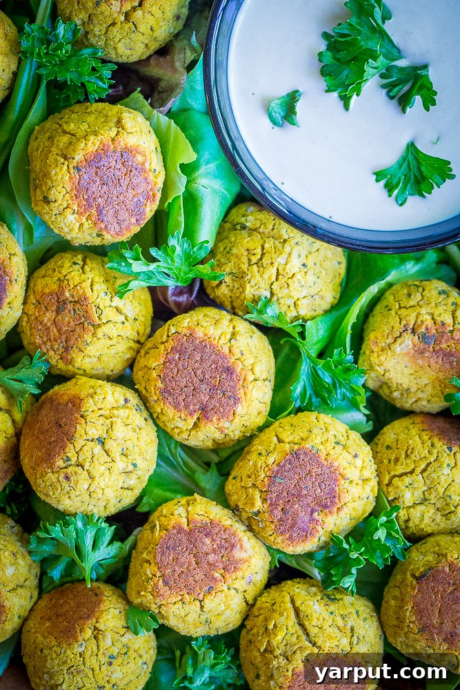 A delightful serving platter featuring a bed of fresh mixed greens, topped with golden-brown roasted butternut squash falafel bites, and a small ceramic bowl filled with creamy citrus tahini dipping sauce.