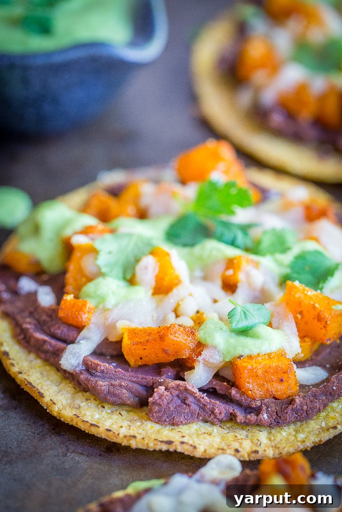Vibrant Roasted Butternut Squash Tostadas with creamy Avocado Lime Sauce and fresh cilantro on a white plate, showcasing a healthy, vegan, and gluten-free Mexican-inspired fall dinner option.