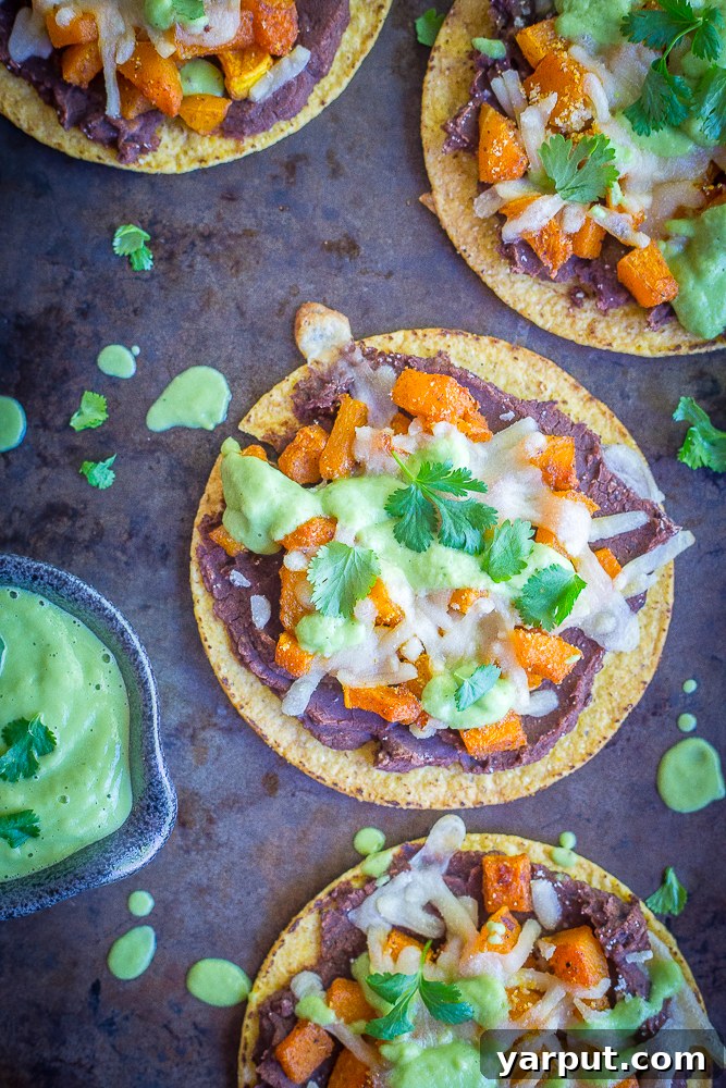 A top-down view of two freshly prepared Roasted Butternut Squash Tostadas with Avocado Lime Sauce and cilantro, placed on a white cutting board, highlighting the vibrant colors and appealing texture of this healthy and easy vegan meal.