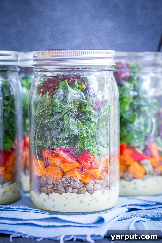 Sweet Potato, Lentil, Kale Prep Bowls with Curry Tahini 5 Four mason jars filled with layered Sweet Potato, Lentil, and Kale Meal Prep Salads, topped with dried cranberries, sitting neatly on a wooden board, ready for the week's healthy lunches.