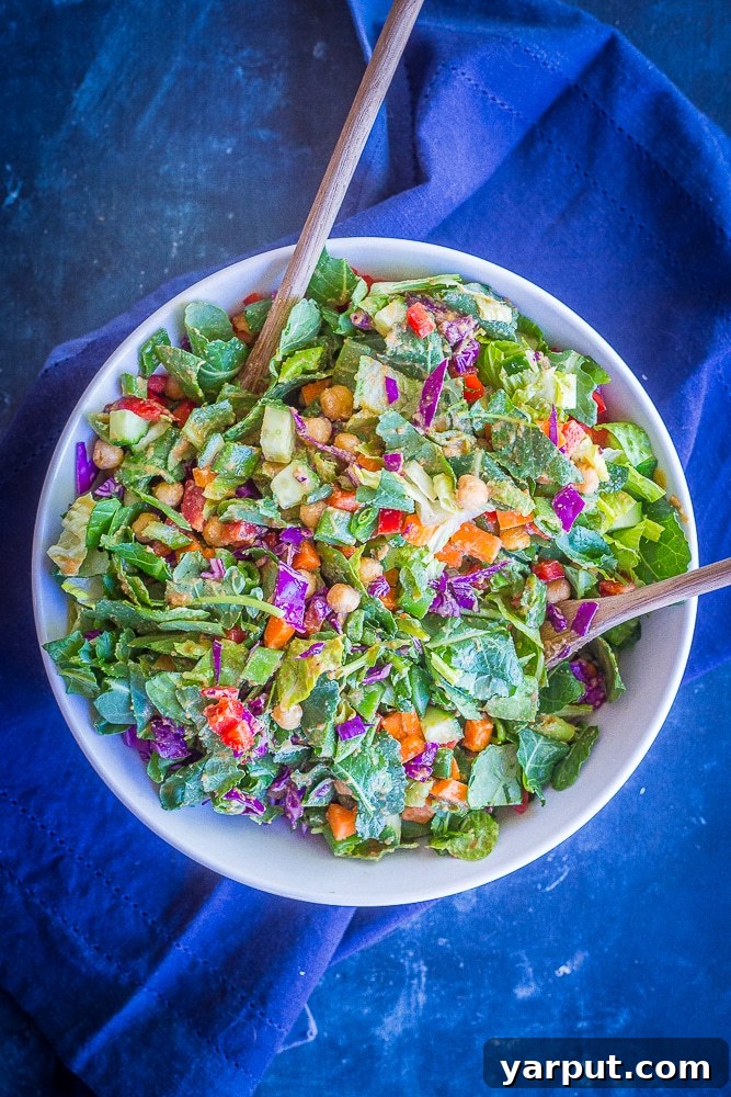 The vibrant Asian Chickpea Chopped Salad, fully mixed and ready to be served, in a large mixing bowl with two rustic wooden serving spoons, showcasing the uniform chop and rich coating of dressing.