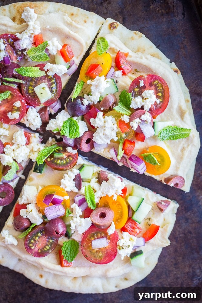 A no cook Mediterranean Hummus Pizza cut into four slices on a sheet pan, showcasing fresh vegetables and a creamy hummus base
