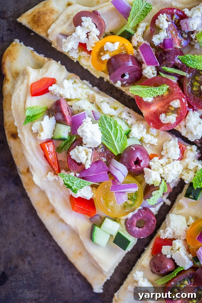 A close-up view of a single slice of No Cook Mediterranean Hummus Pizza, ready to be enjoyed