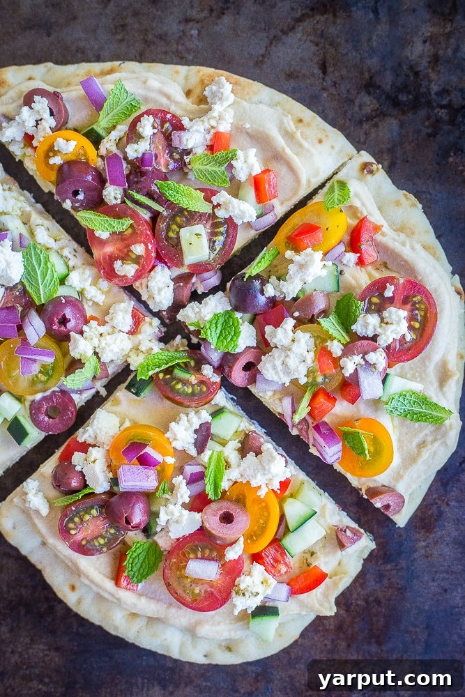 A No Cook Mediterranean Hummus Pita Pizza sliced into four portions on a wooden cutting board
