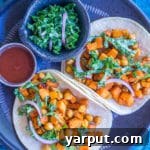 Sweet Potato and Chickpea Tacos on a plate with fresh lemony kale slaw and a drizzle of hot sauce.