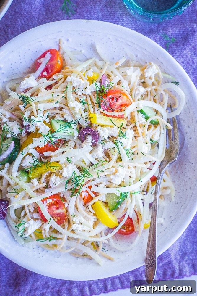 Mediterranean Kohlrabi Noodle Salad 2 A beautifully arranged bowl of Healthy Greek Pasta Salad with Kohlrabi Noodles, featuring a mix of colorful vegetables and a creamy dressing, set on a white bowl against a purple napkin.