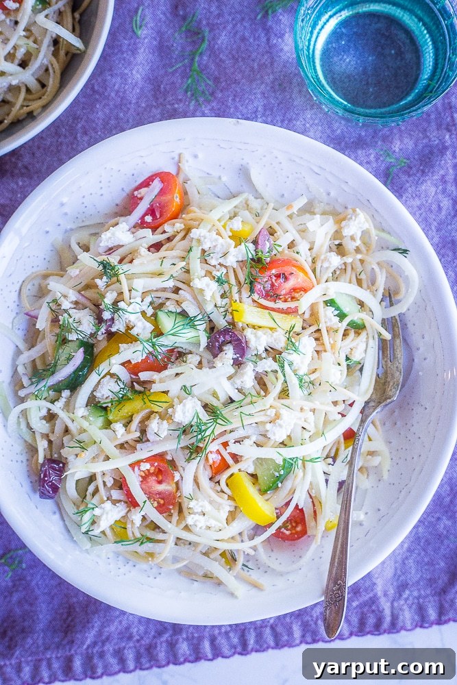 Mediterranean Kohlrabi Noodle Salad 5 A close-up shot of a bowl of Healthy Greek Pasta Salad with Kohlrabi Noodles, highlighting the fresh ingredients and the appealing texture, on a white bowl over a purple napkin.