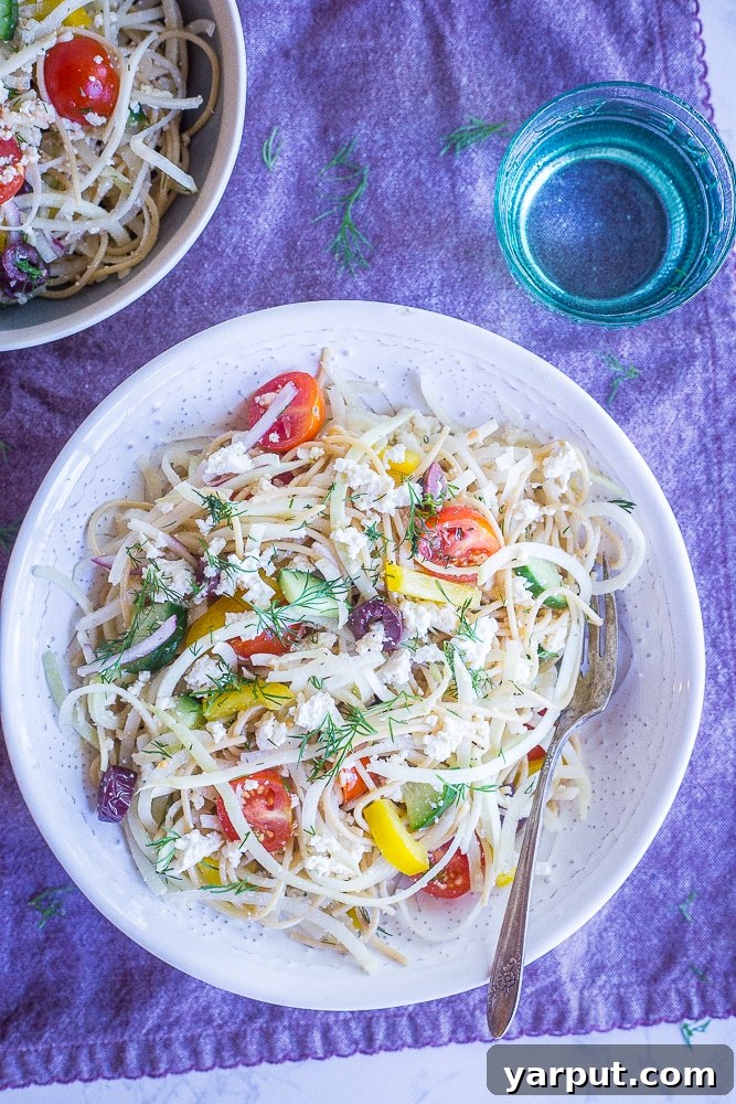 Mediterranean Kohlrabi Noodle Salad 7 A bowl of Healthy Greek Pasta Salad with Kohlrabi Noodles, brimming with fresh ingredients and a delightful dressing, sitting on a white bowl atop a purple napkin.