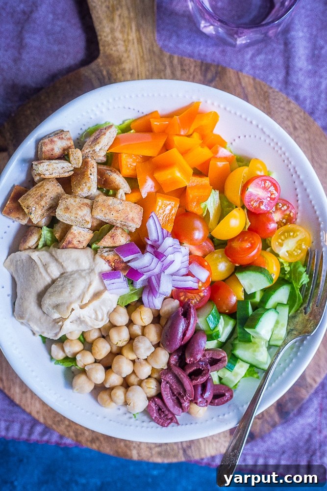 Grab-and-Go Greek Salad Prep Bowls 5 A big bowl of Easy Greek Salad Meal Prep Bowls on a wooden cutting board with a purple napkin.