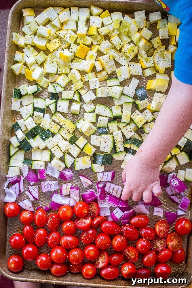 Roasted Summer Harvest Meal Prep Bowls 3 An array of colorful summer vegetables including zucchini, summer squash, cherry tomatoes, and red onion, seasoned and ready for roasting on a large baking sheet, destined for delicious meal prep bowls.