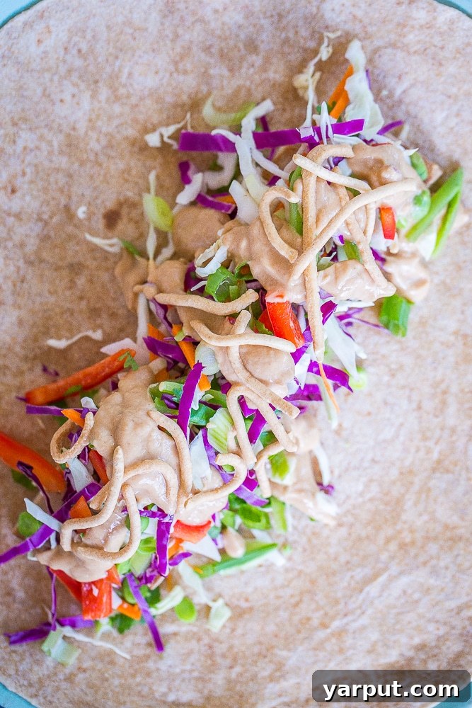 An open Crunchy Asian Tofu Peanut Wrap on a plate, revealing a colorful medley of vegetables, golden tofu strips, and noodles.