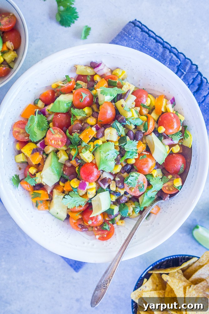 Summer Harvest Black Bean Salad 4 A beautifully composed flat lay of the Loaded Summer Vegetable Salad with Black Beans in a large serving bowl, surrounded by fresh ingredients and tortilla chips on a rustic blue surface.
