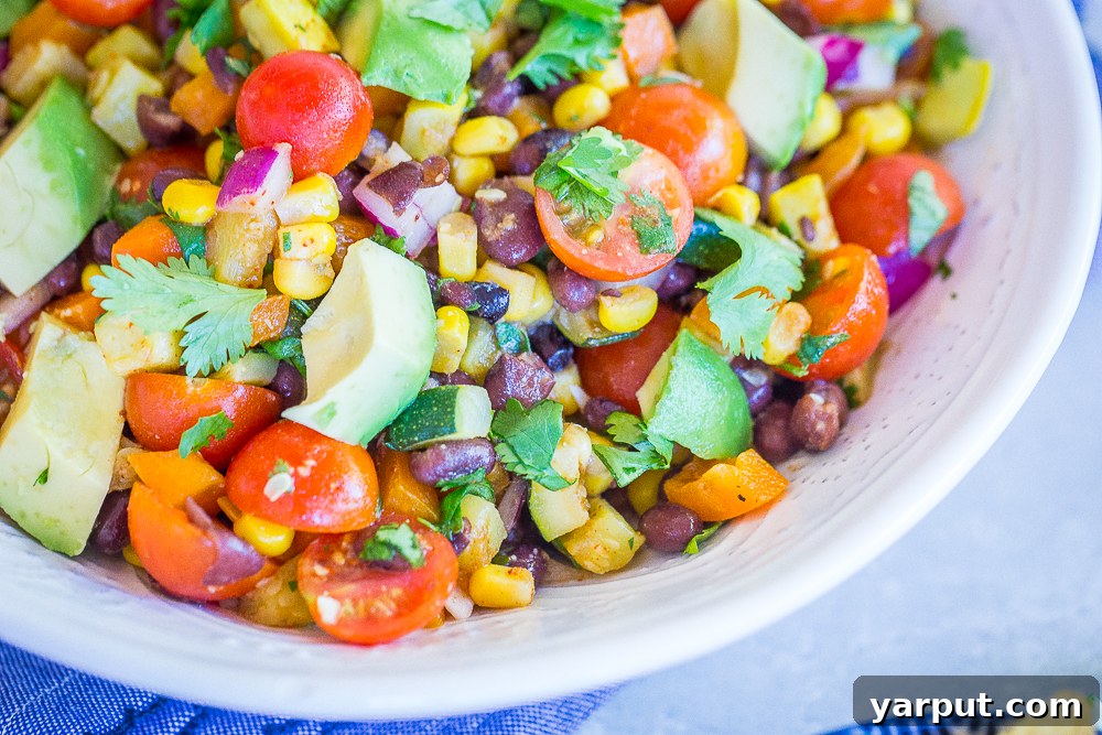 Summer Harvest Black Bean Salad 5 A vibrant and generously sized bowl of Loaded Summer Vegetable Salad with Black Beans, placed on a blue textile with crispy tortilla chips, ready for serving at a summer gathering.