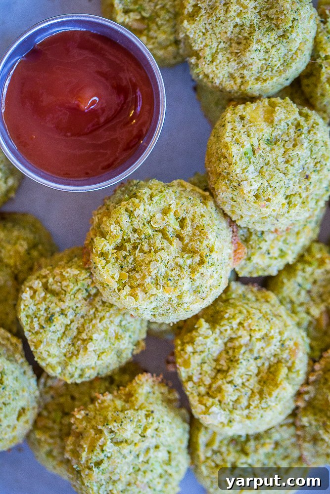 Broccoli Cheddar Power Poppers 3 A close-up shot of several Protein-Packed Broccoli Cheese Bites piled on a white plate, with a dollop of ketchup on the side, highlighting their crispy texture and cheesy interior.