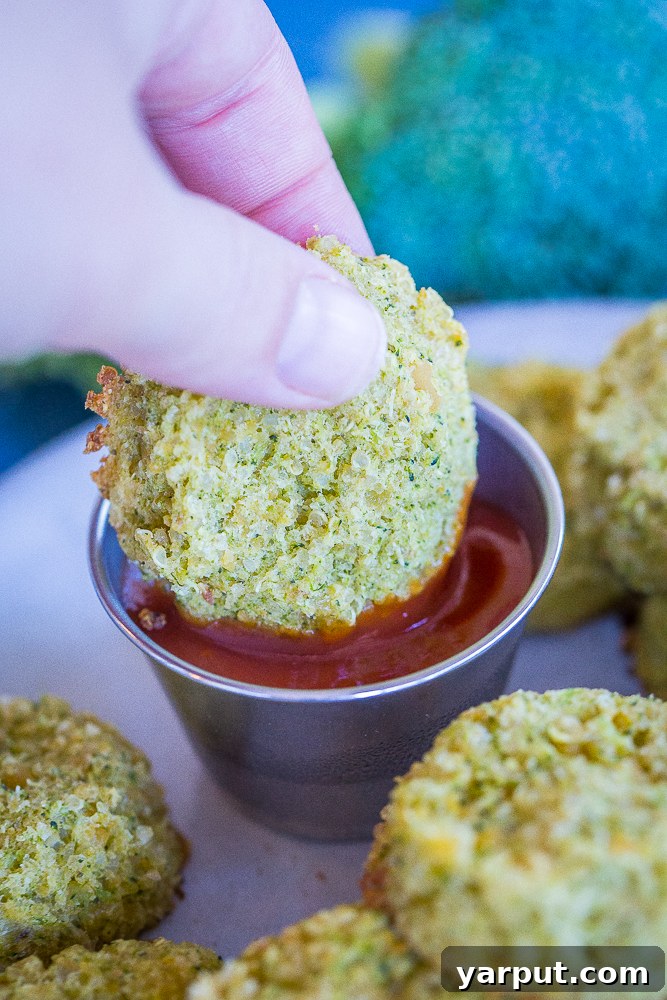 Broccoli Cheddar Power Poppers 4 A hand is shown dipping a golden-brown Protein-Packed Broccoli Cheese Bite into a small white bowl of red ketchup, emphasizing the snack's appeal and deliciousness.