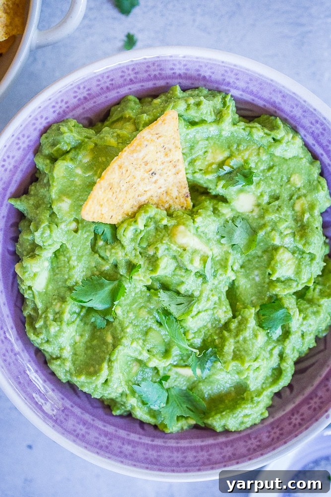 Perfect Guacamole Made Simple 3 A close-up shot of a bowl of The Best Easy Guacamole in a purple bowl, with a single tortilla chip already dipped in, ready to be enjoyed.