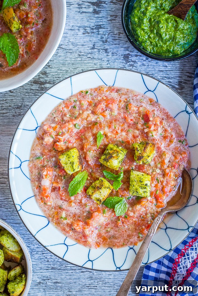 Two vibrant bowls of chunky cherry tomato gazpacho, garnished with fresh mint pesto croutons, sitting on a rustic wooden surface. Perfect for a hot summer day.