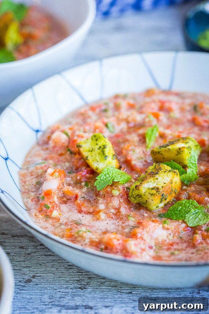 A large, inviting bowl of chunky cherry tomato gazpacho, topped with fresh herbs and a drizzle of olive oil, ready to be enjoyed as a cool summer meal.