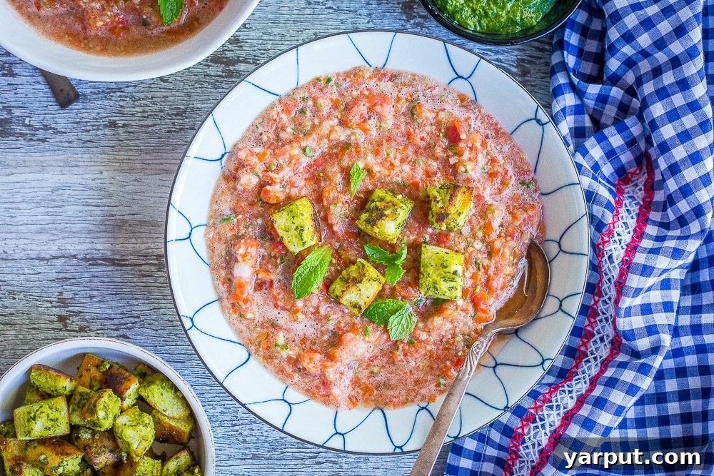 Two close-up bowls of vibrant chunky cherry tomato gazpacho, generously topped with crispy homemade mint pesto croutons, inviting a refreshing summer meal.