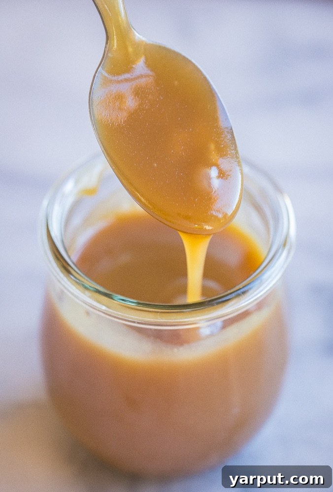 Silky Tahini Maple Vegan Caramel 6 a spoon being dipped into a jar of salted caramel sauce, ready to be enjoyed