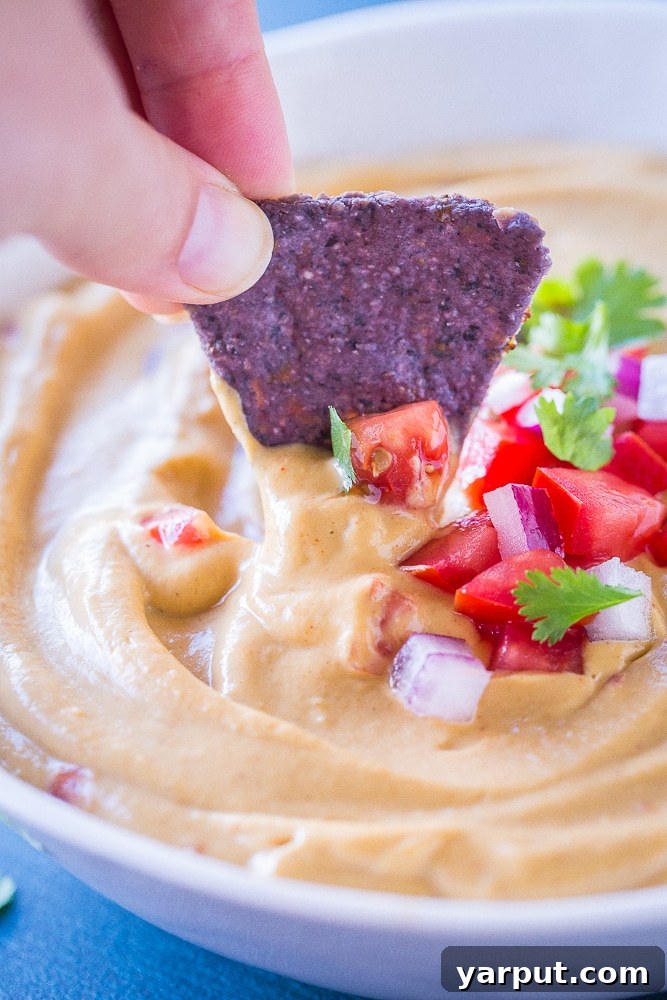 A tortilla chip being dipped into a luscious bowl of Creamy Cauliflower Queso Dip