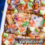 A close-up shot of a single serving of Black Bean Enchilada Casserole, topped with fresh avocado and cilantro.