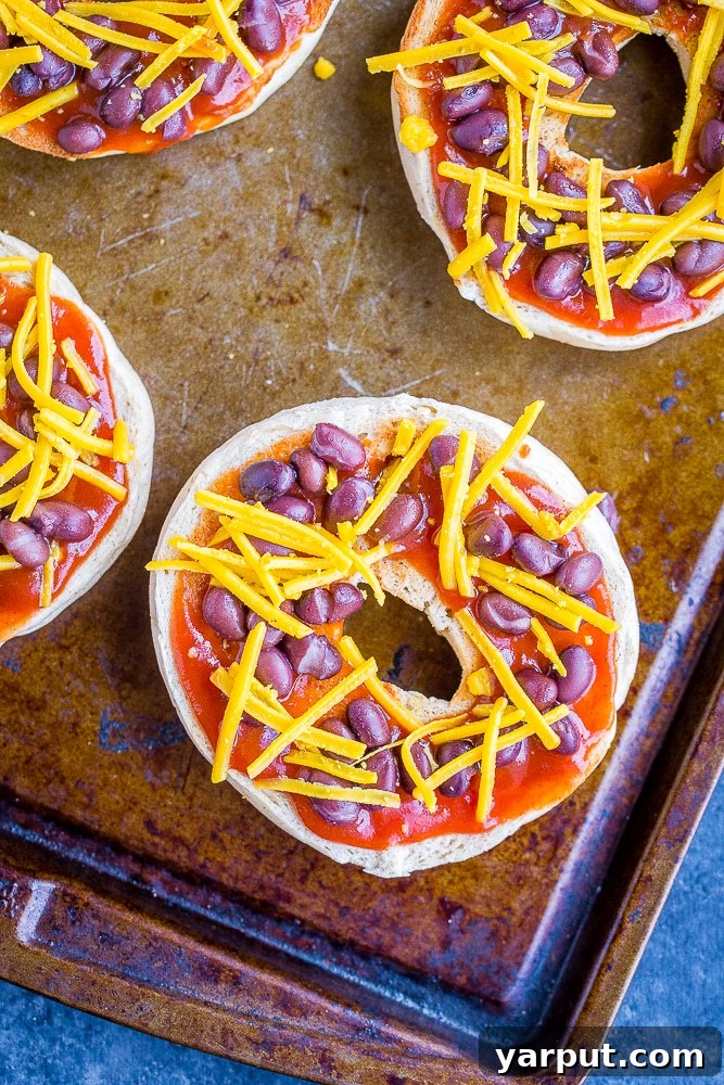 Fiesta Pizza Bagels 3 Sheet pan filled with unbaked Taco Pizza Bagels, topped with taco sauce, black beans, and shredded cheese, ready for the oven.