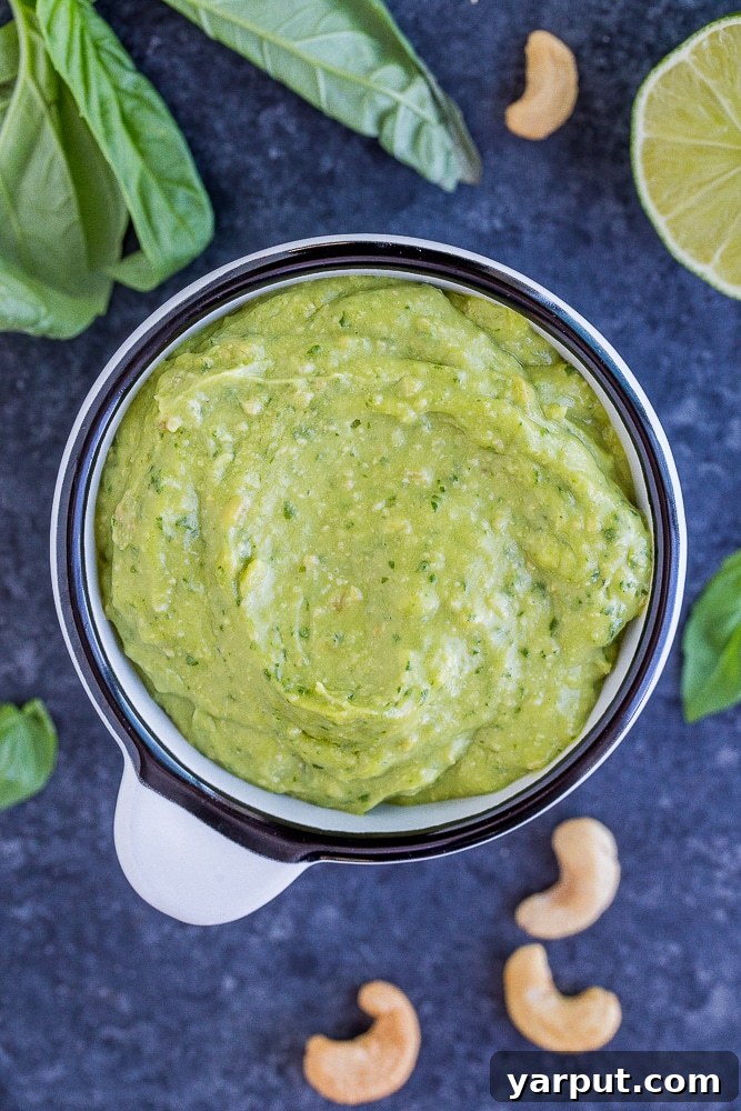 Whip Up Delicious Avocado Pesto 5 Avocado Pesto Sauce in a bowl, surrounded by fresh ingredients like basil, lime, garlic, and cashews, ready for blending.