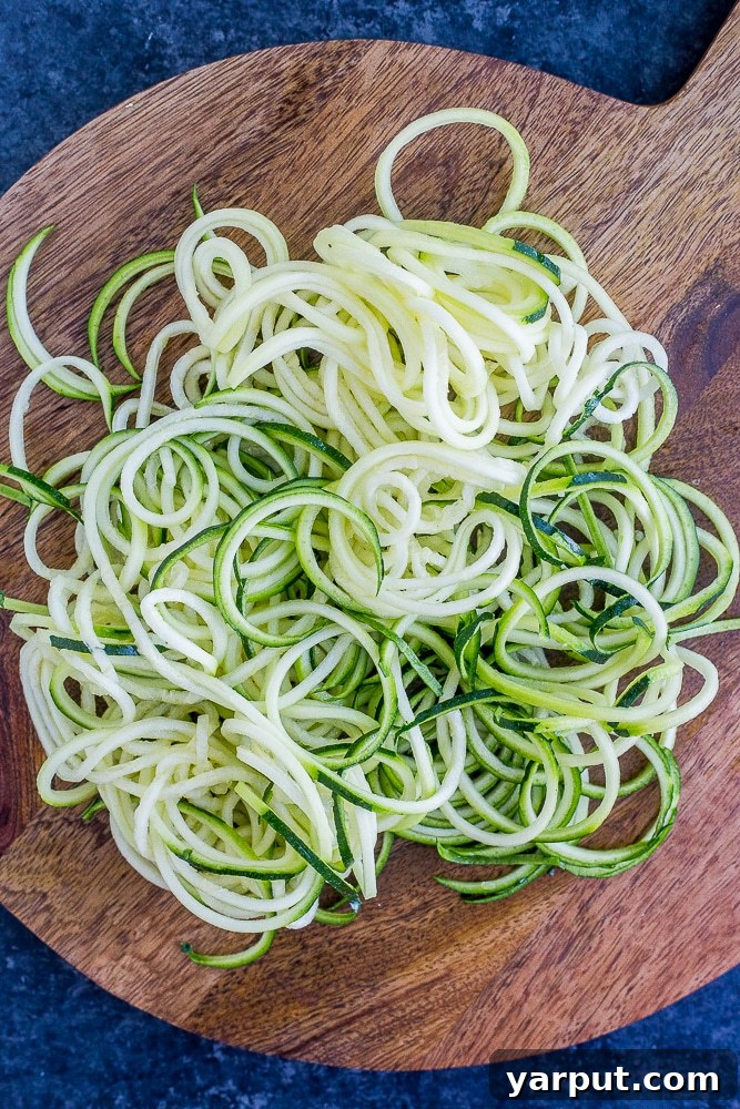 20 Minute Creamy Avocado Pesto Zucchini Noodles 4 Freshly spiralized zucchini noodles laid out on a cutting board, alongside cooked whole wheat spaghetti, prepared for combining.