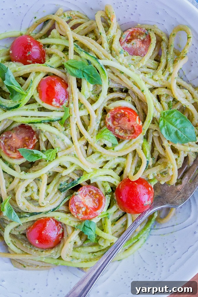 20 Minute Creamy Avocado Pesto Zucchini Noodles 6 A close-up view of a serving of Avocado Pesto Zucchini Noodles in a bowl, showing the creamy pesto, green zoodles, and red cherry tomatoes.