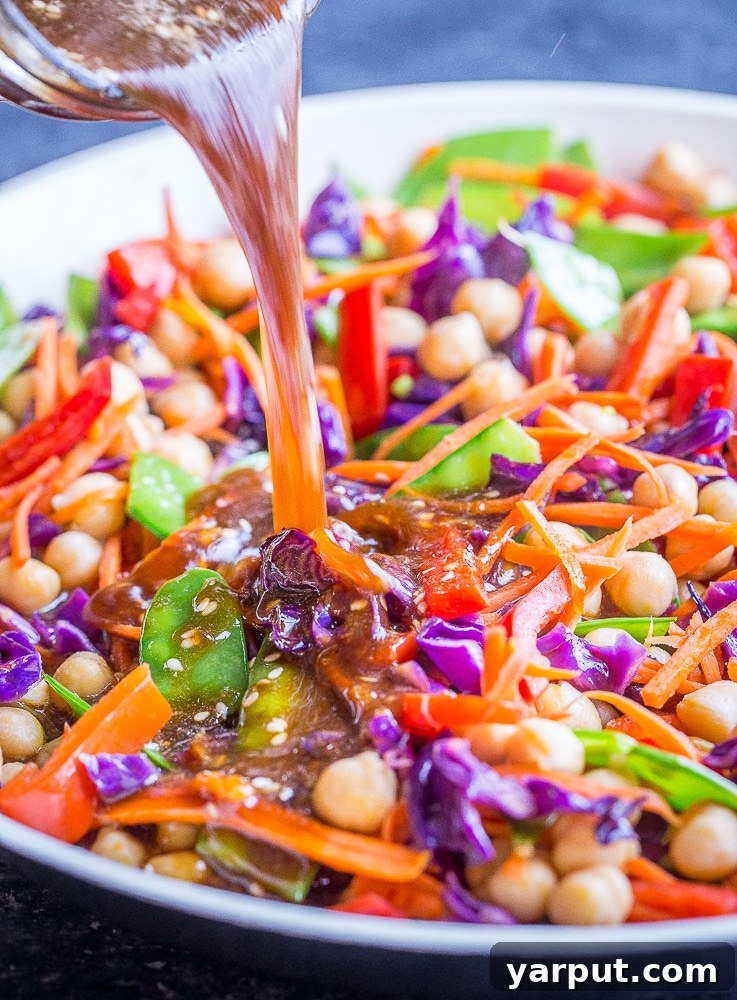 The Perfect Wholesome Stir Fry Sauce 5 Pouring the best stir fry sauce over a pan of vibrant stir-fry vegetables, showing how the sauce coats them evenly.