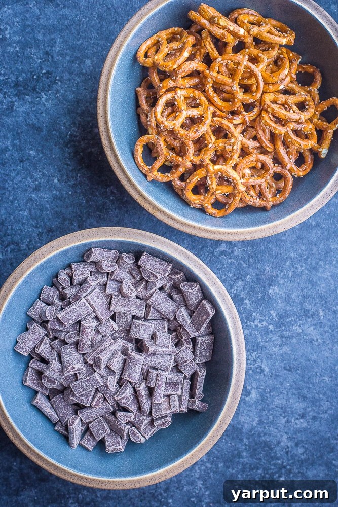 A ceramic bowl filled with dark chocolate chunks and crispy pretzels, awaiting their transformation into delicious chocolate bark.