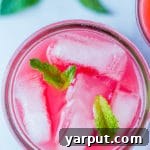 A close-up of a glass of watermelon juice garnished with mint, with sliced watermelon in the background.