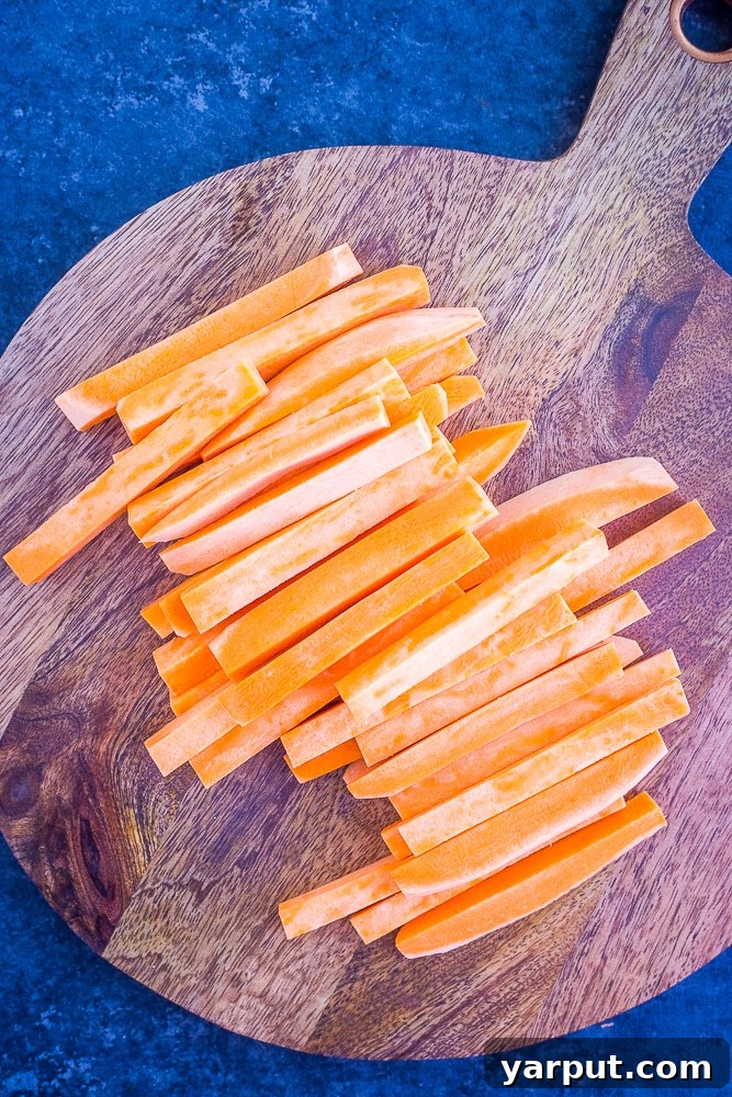 Golden Crispy Baked Sweet Potato Fries 3 Fresh sweet potatoes precisely cut into fry shapes, ready for seasoning and baking, on a rustic cutting board