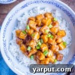 A bowl of Vegan Orange Tofu on rice, garnished with green onions and sesame seeds.