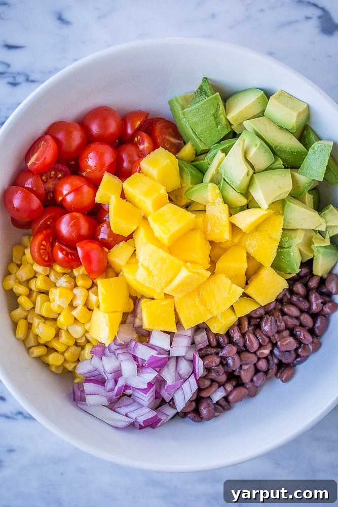 Close-up of fresh ingredients in a bowl, including black beans, corn, diced mango, avocado, and cherry tomatoes, ready to be mixed for Black Bean Salad with Mango and Avocado.