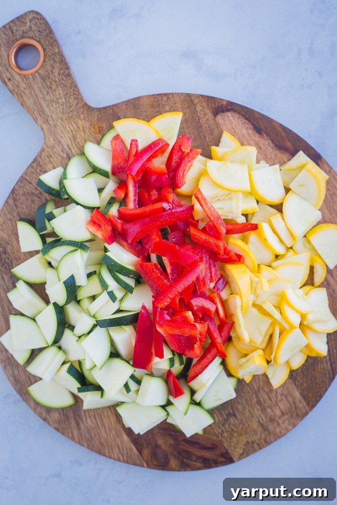 Vibrant Summer Pesto Pasta 3 Freshly diced summer vegetables, including vibrant green zucchini, sunny yellow summer squash, and bright red bell peppers, neatly arranged on a wooden cutting board, ready for the pesto pasta recipe.