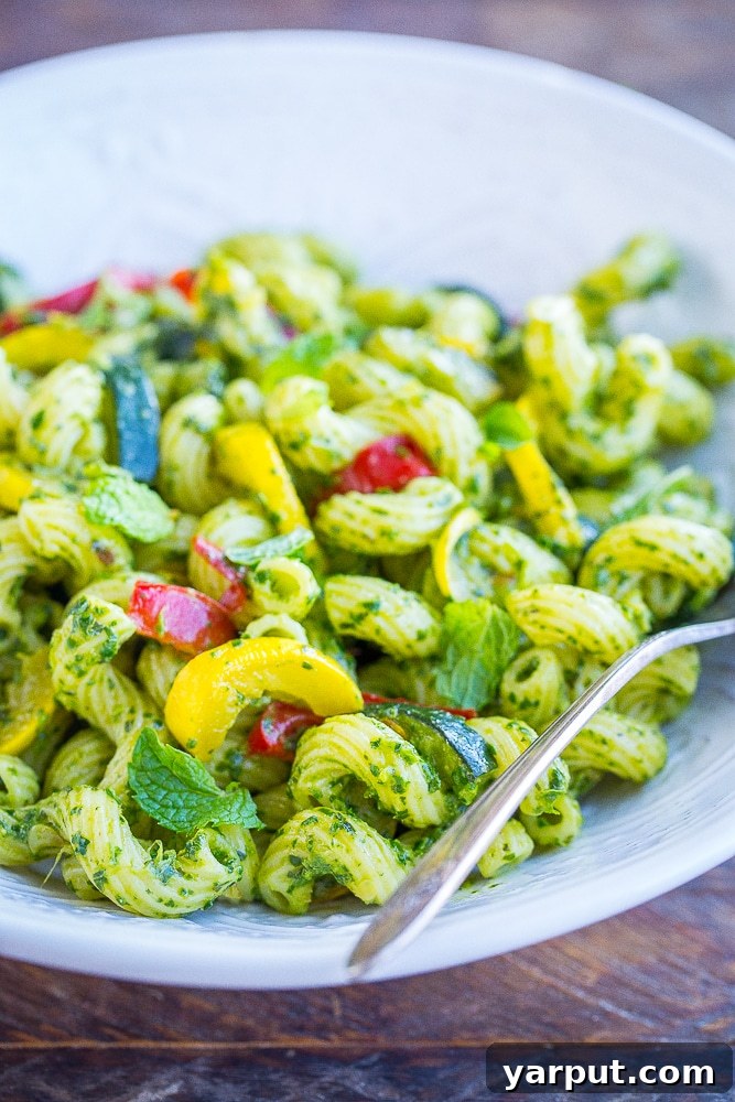 Vibrant Summer Pesto Pasta 5 A vibrant close-up of Pesto Pasta with Summer Vegetables, showcasing perfectly coated pasta strands, glistening pieces of browned zucchini, yellow squash, and red bell pepper, all infused with rich green pesto and garnished with fresh herbs, ready to be enjoyed.