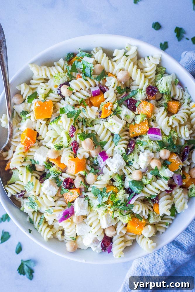 A large, inviting bowl of Fall Pasta Salad, generously filled with golden roasted butternut squash, vibrant green broccoli florets, creamy white feta chunks, and ruby-red dried cranberries, artfully arranged for an autumn feast.