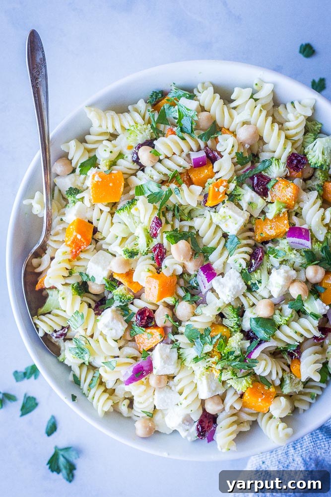 A close-up, irresistible view of the Fall Pasta Salad in a shallow bowl, highlighting the rich textures and vibrant colors of the roasted butternut squash, crisp broccoli, creamy feta, and chewy dried cranberries, all glistening with the tangy dressing.