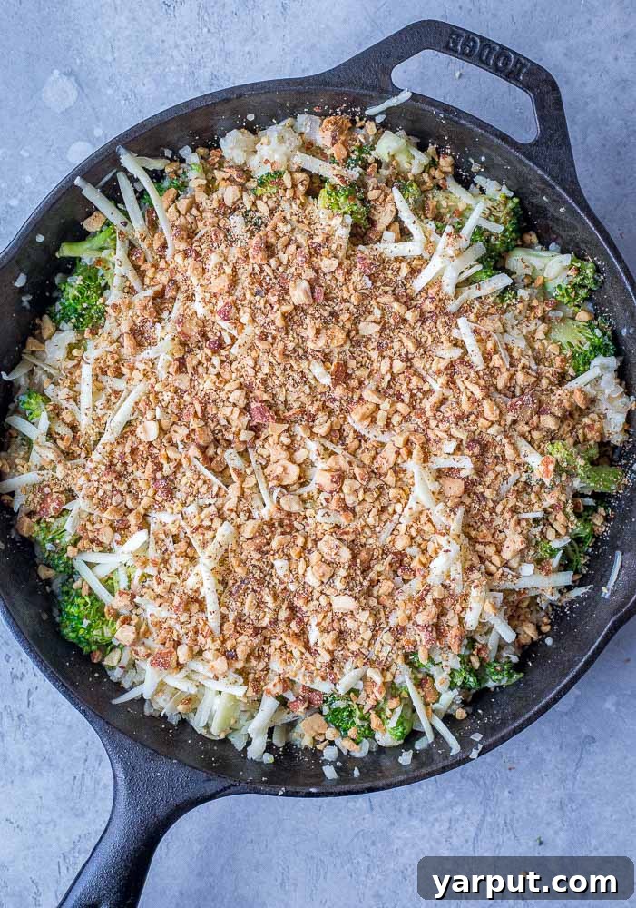 A casserole dish filled with uncooked broccoli cheese mixture, topped with cheese and almonds, ready for the oven.