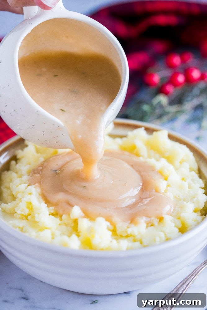 Effortless & Flavorful Vegan Gravy 2 Rich, creamy vegan gravy being poured generously over a mound of fluffy mashed potatoes, highlighting its perfect consistency and inviting warmth.