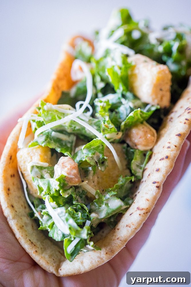 Caesar Kale Pita Pockets 7 Close up of a hand holding a freshly made Kale Caesar Salad Pita, highlighting its substantial and inviting filling.