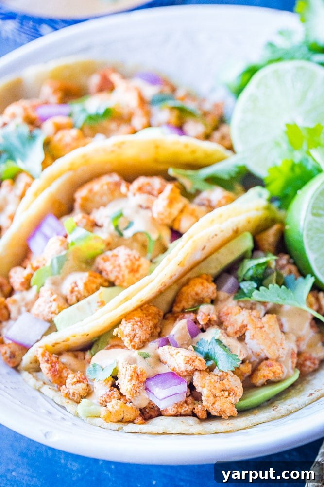 Tahini Cheesy Vegan Tacos 4 Close-up shot of several vegan tacos, filled generously with tofu and walnut meat, topped with avocado, red onion, cilantro, and drizzled with tahini cheese sauce, highlighting the delicious textures.