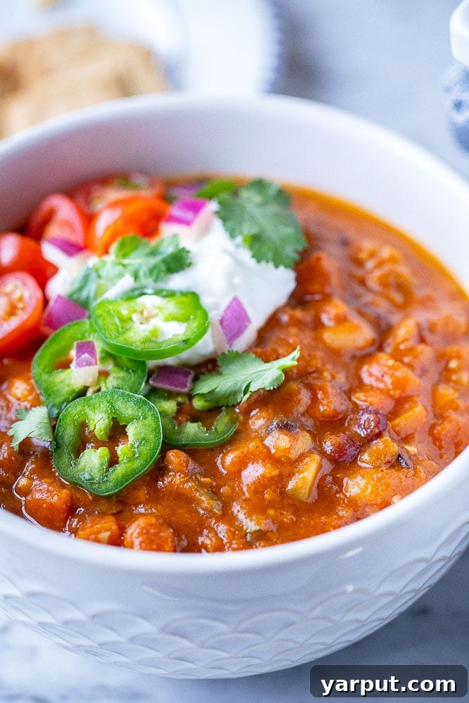 A close-up shot of a single serving of the best vegetarian chili in a rustic bowl, garnished with a swirl of sour cream, fresh cilantro, and a sprinkle of cheese, inviting a comforting meal.