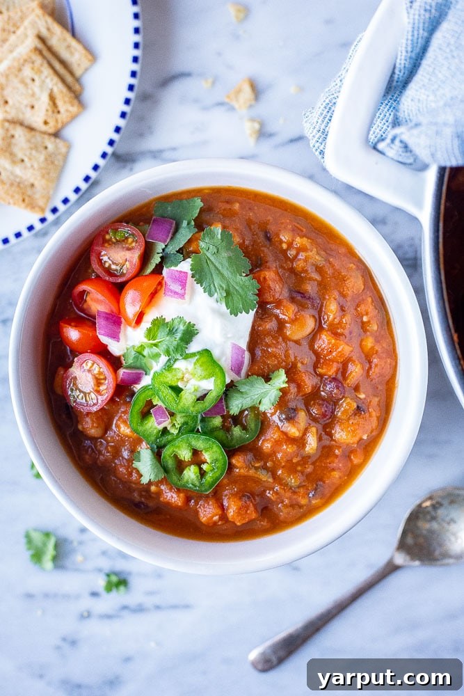 A beautifully arranged flatlay photo of a bowl of vegetarian chili, surrounded by an assortment of colorful toppings like crackers, avocado, and cilantro, highlighting the customizable nature of the dish.