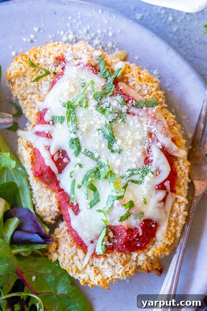 Golden Parmesan Cauliflower 5 A close-up view of a serving of Cauliflower Parmesan, showing the thick, crispy coating, rich marinara, and melted mozzarella cheese, with a fresh salad in the background.