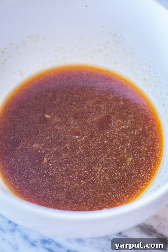 A bowl of sesame noodle sauce being prepared, showing a whisk and various liquid ingredients