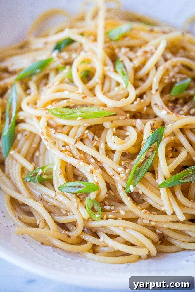 Close up of a serving of sesame noodles in a white bowl, garnished with green onions